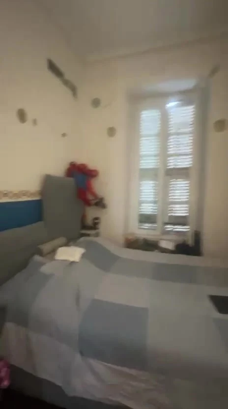 État actuel avant travaux : chambre meublée et porte-fenêtre à volets, image extraite de la vidéo.